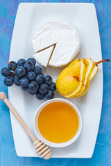 Cheese brie (camembert) with honey and fruits on a white plate.