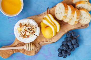 Brie cheese (camembert) with honey, nuts and fruits on a wooden board.