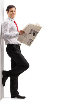 Formally dressed man with a newspaper leaning against a wall
