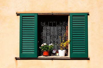 Old wooden windows frame on stone wall with flowers in Italy.