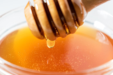 Honey dripping from honey dipper on white background. Thick honey dipping from the wooden honey spoon. Healthy food concept.