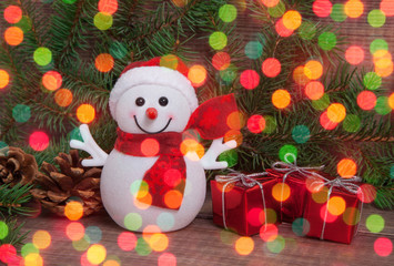 Christmas background with snowman,  fir tree branches, cones, gifts with copy space and glowing lights, bokeh. New year backdrop.
