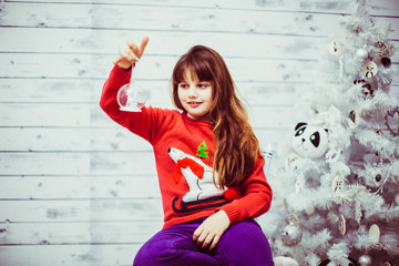 Little girl in orange sweater plays with toys before a white Christmas tree