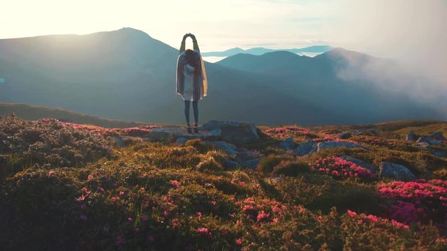 Back view of fit woman in boho look practicing yoga while standing on the mountain top, enjoying the moment and observing the distant hills, forest. Harmony, relaxation, happiness.