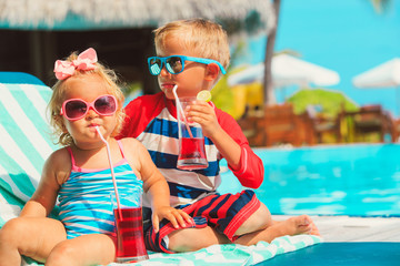 little boy and toddler girl drinking juices on beach