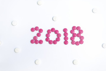 Number 2018 made from pink pharmaceutical pill with white tablets in background.