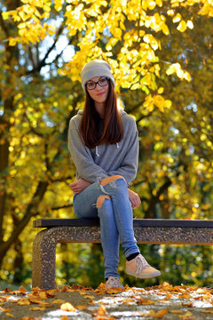 Caucasian girl with long hair sitting on bench in autumn park