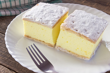 Cream pie with layers of puff pastry in plate on wooden table