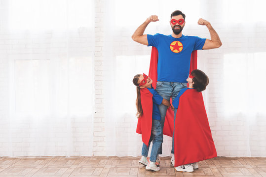 Father with children in red and blue suits of superheroes. They in masks and in raincoats.