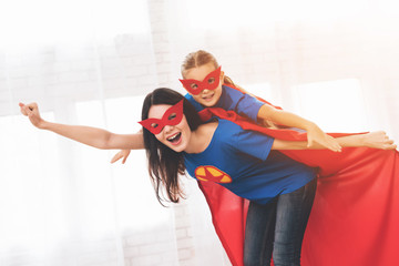 Mother with doughter in red and blue suits of superheroes. They in masks and in raincoats.