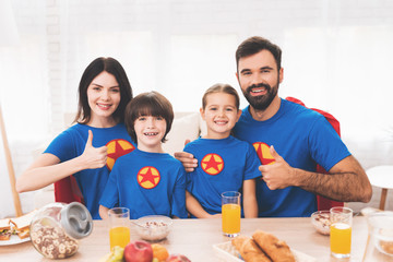 A family of superheroes sit at a table. The incredibles are posing in a bright room