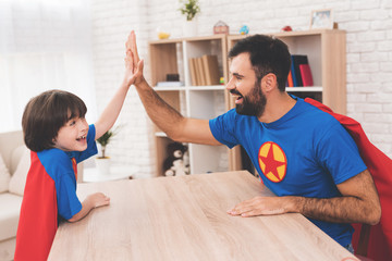 Fototapeta premium Father and son in suits of superheroes. They compete in arm wrestling.