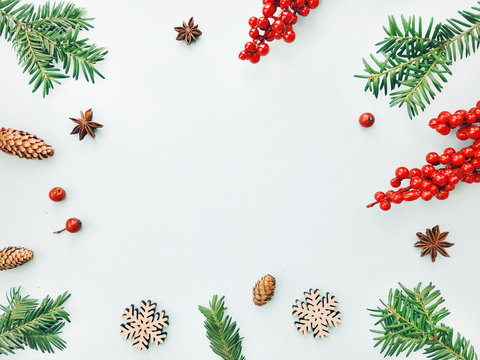 Christmas background. Frame made of christmas tree branches, red berries, pine cones and wooden snowflakes. Flat lay, top view, copy space
