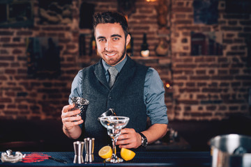 Smiling barman, professional waiter looking at camera and preparing cocktail