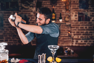 Smiling barman using shaker for cocktail preparation. Portrait of barman making tequila based margarita at local pub