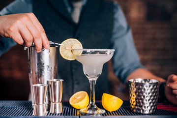 Bartender garnishing drink, pouring fresh lime margarita in fancy glass at restaurant