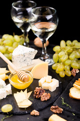 Cheese plate. Assortment of cheese with walnuts, bread an honey on stone slate plate.