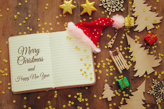 Top view image of christmas festive decorations next to open notebook on old wooden background.
