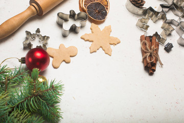 Gingerbread cookies making concept, selective focus, top view, raw dough ball on table with wooden roller, tree man snowflake shape cutters, green pine branches on white table with flour, decoration
