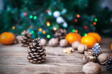Pine cones, tangerines, Walnuts, christmas tree and holiday colored lights on wooden background. Christmas and New Year card with copy space