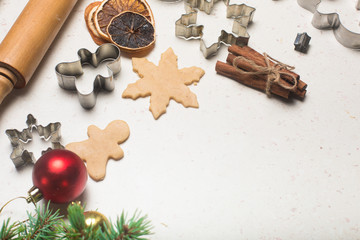 Gingerbread cookies making concept, selective focus, top view, raw dough ball on table with wooden roller, tree man snowflake shape cutters, green pine branches on white table with flour, decoration