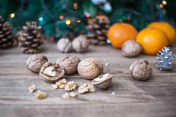 Walnuts and blurred background with orange mandarines, cones, christmas tree and holiday lights on wooden table. Christmas and New Year concept
