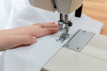 Hand eines Kindes führt einen weißen Stoff über die Nähmaschine. Eine Naht wird genäht, Nahaufnahme