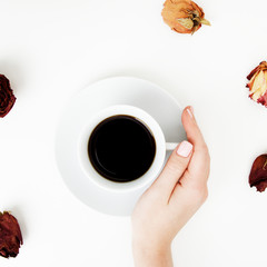 Flat lay. Top view. Minimal style. Minimalist Fashion and beauty photography. Morning mood. A girl with manicure holds a white cup of coffee on a white table background. Rose petals around the cup