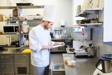 Obraz premium chef with clipboard doing inventory at kitchen
