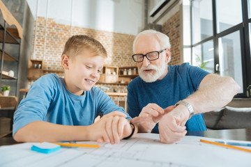 Technological differences. Positive nice cheerful grandfather and grandson sitting together and looking at their watches while comparing their technology