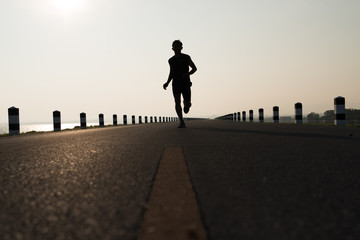 Asia young man running in the time during sunrise on dam road exercise.Healthy lifestyle