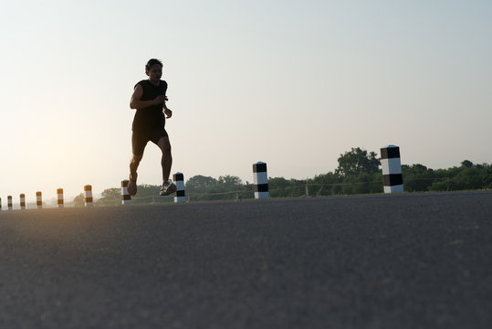 Asia young man running in the time during sunrise on dam road exercise.Healthy lifestyle