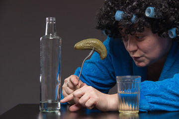 Lonely mature fat woman alcoholic drinks vodka from glasses and wine glasses and snack cucumber and fish