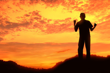 Happy celebrating winning success at sunset or sunrise standing elated with arms rose up above her head in celebration of having reached mountain summit