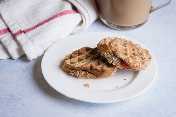 Grilled cheese wholegrain sandwich with tomato and cup of coffee with milk on light table background. Morninig concept