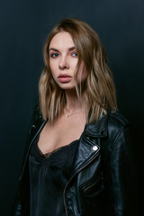 Portrait of the young attractive stylish blonde woman in silk dress and black jacket on the dark background