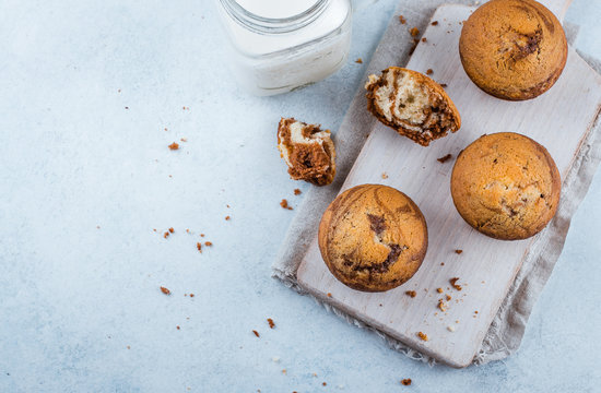 Food Background. Homemade sweet chocolate vanilla muffins from two types of dough with mason jar of milk on on wooden board on blue stone table background