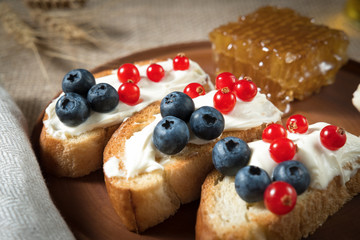 fried bread, toast with yoghurt and berries, bilberries, blueberries and red currants on a wooden plate with honey honeycomb