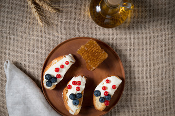 fried bread, toast with yoghurt and berries, bilberries, blueberries and red currants on a wooden plate with honey combs on the background of linen cloth and bottle of oil on the background