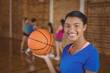 Smiling high school girl holding a basketball while team playing