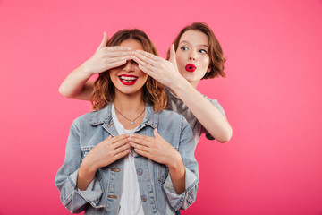 Two women friends covering eyes with hands.