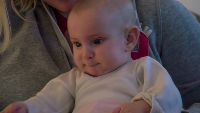 Young mom is pulling down dirty pink baby`s pants meanwhile little baby girl is sitting in mom`s lap.