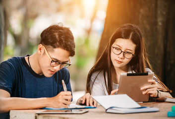 A group of young or teen asian student in university smiling and reading the book and look at the tablet or labtop computer in summer holiday.