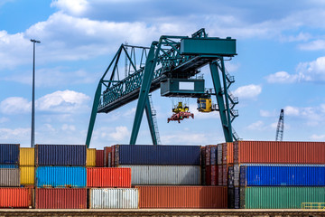 Grüner Lastenkran schwebt über gestapelten Containern im Containerhafen