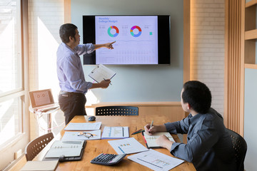 Businessman present the monthly college budget in front of TV to his colleagues during meeting
