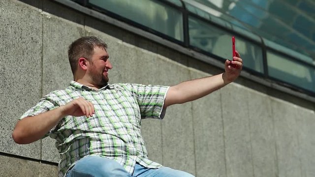 Man makes selfie on smartphone. Man makes photos on his red cell phone