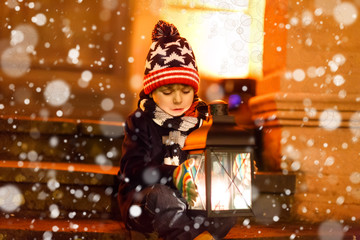 Little cute kid boy with with a light lantern on stairs near church.