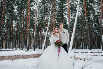 Bride and groom with a bouquet are posing on background of the snowy forest. Winter wedding. Artwork