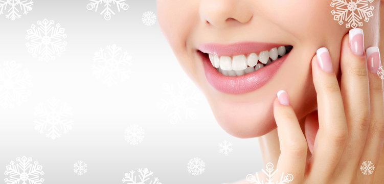 Closeup shot of woman's toothy smile against a grey background with snowflakes