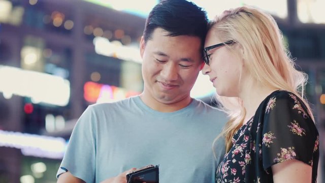 A young multi-ethnic couple uses a smartphone. Night city against a background of blurry lights